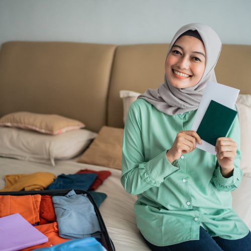 veiled woman sitting on the bed and holding a ticket while smile looking at the camera
